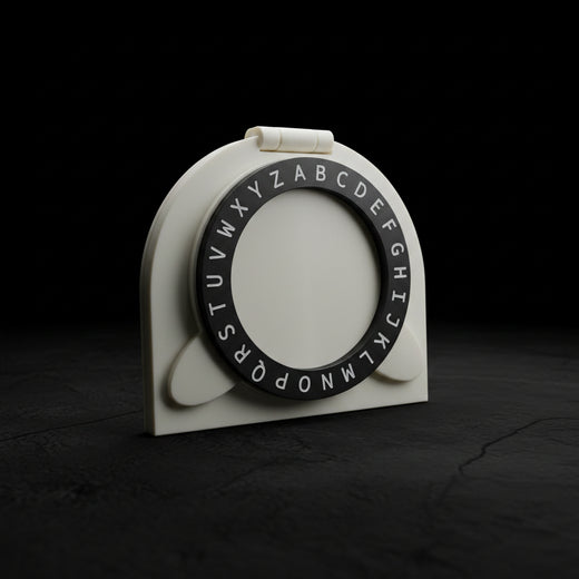 A white plastic alphabet ring holder with a black circular ring printed with uppercase alphabet letters, resting on a dark brown wooden table.