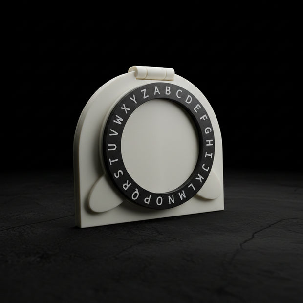 A white plastic alphabet ring holder with a black circular ring printed with uppercase alphabet letters, resting on a dark brown wooden table.