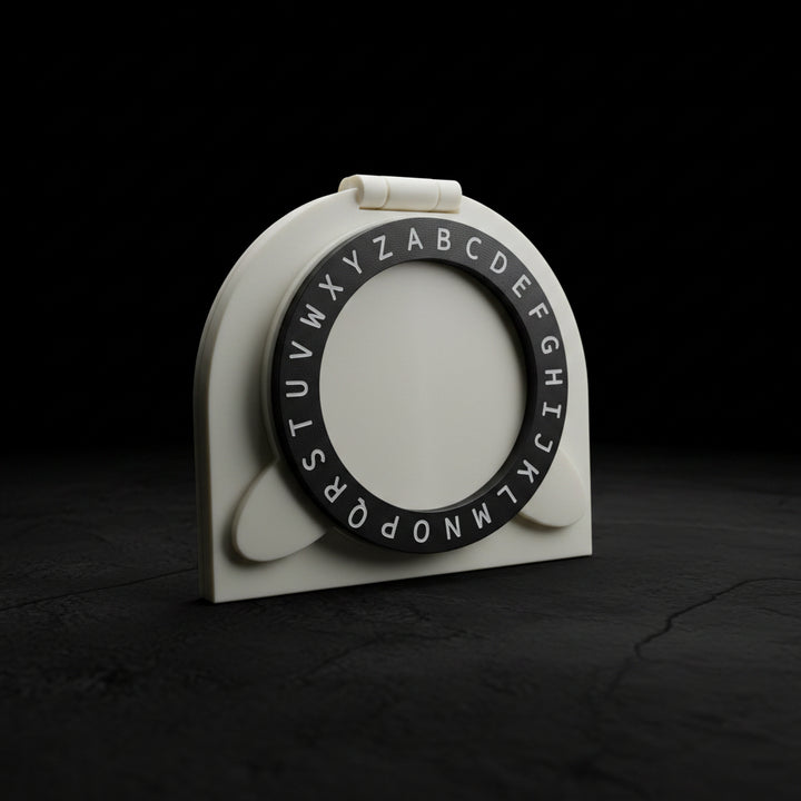 A white plastic alphabet ring holder with a black circular ring printed with uppercase alphabet letters, resting on a dark brown wooden table.