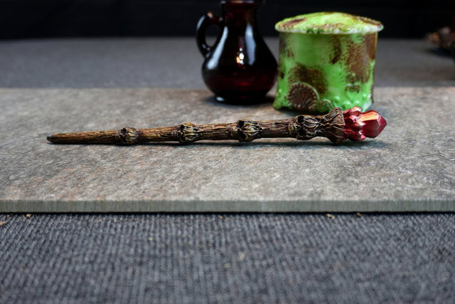 Wooden wand with red gemstone and green mossy object on gray surface.