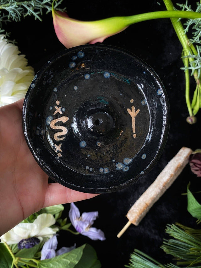 Black ceramic dish with floral and plant elements on a dark background