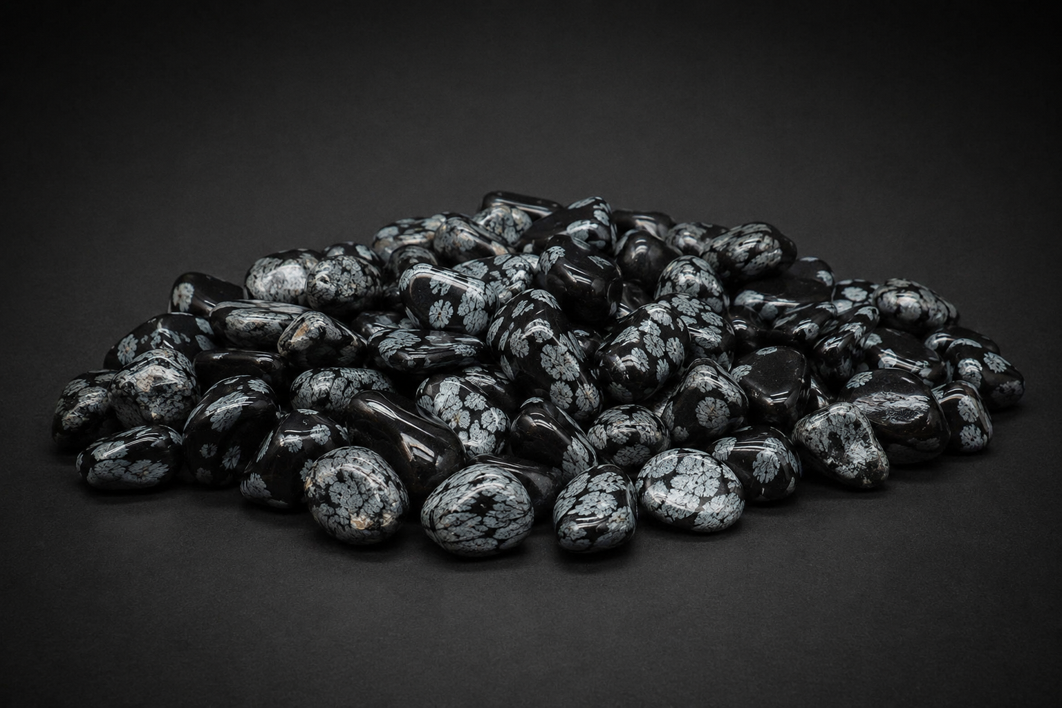 Pile of polished black Snowflake Obsidian tumbled stones with gray-white cristobalite patterns on black