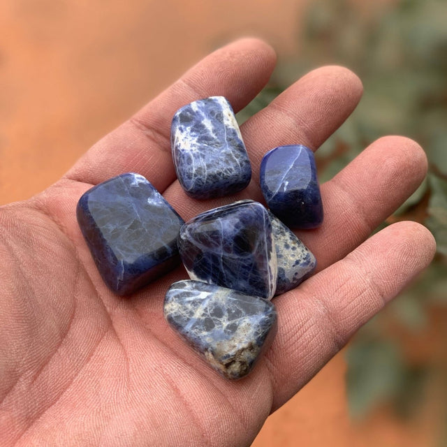 Hand holding five blue and purple gemstones with a blurred natural background