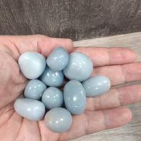 Hand holding a small pile of light blue stones against a neutral background
