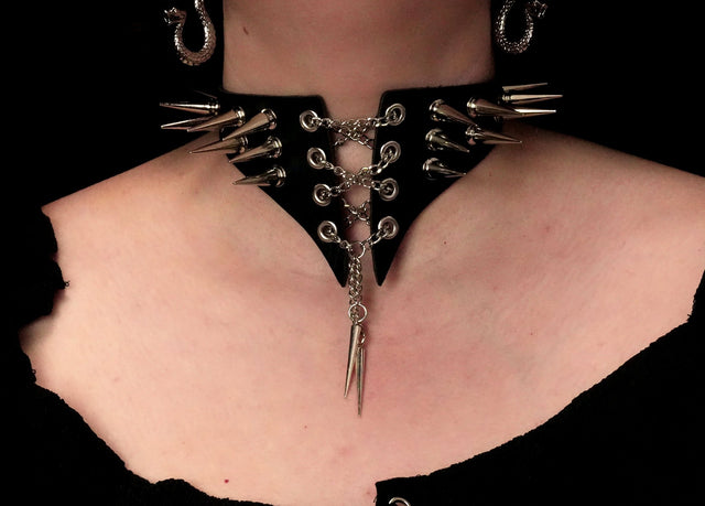 A close-up image of a spiked leather choker collar with metal spikes and a snap fit, worn around the neck.