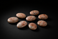 Eight polished peach and cream Sunstone palm stones with varied feldspar mottling on black