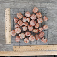Pile of pink stones on a gray surface with rulers for scale.
