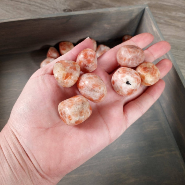 Hand holding orange and white stones over a metal container