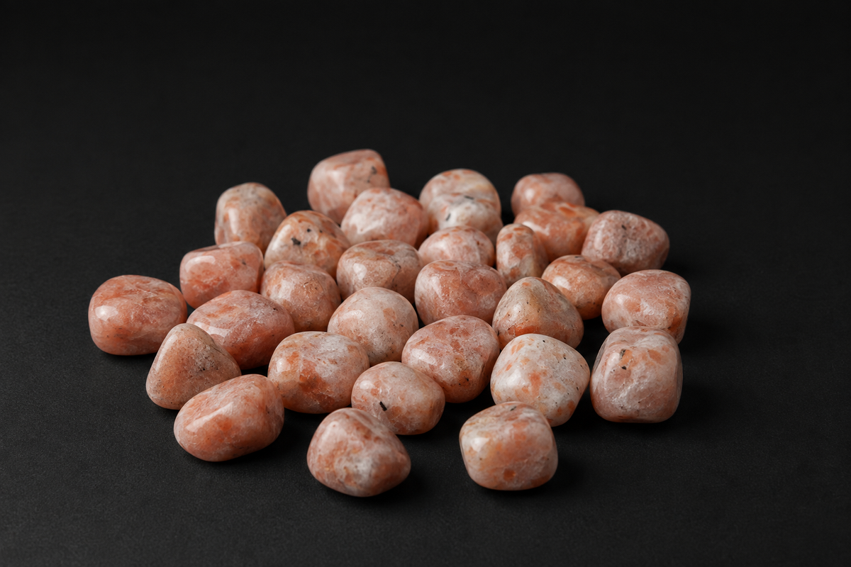 Assortment of polished peach and cream Sunstone tumbled stones with subtle dark inclusions on black