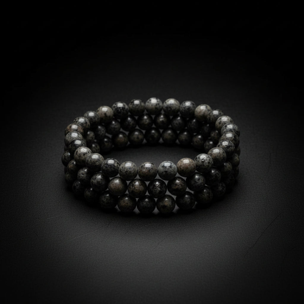 A close-up of few strands of dark gray to black round beads, likely stone or ceramic, against a gray wood background.
