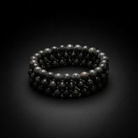 A close-up of few strands of dark gray to black round beads, likely stone or ceramic, against a gray wood background.