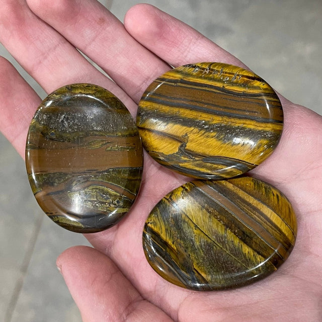 Three tiger's eye stones held in a hand with a neutral background