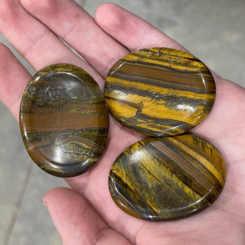 Three tiger's eye stones held in a hand with a neutral background