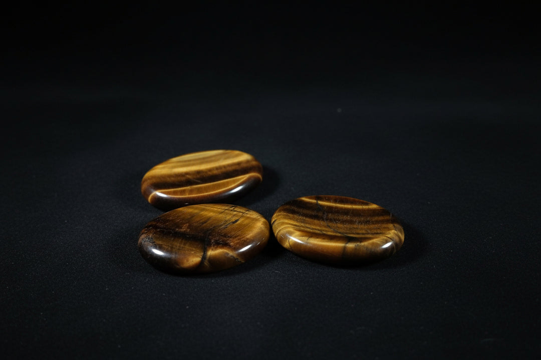 Assorted polished golden-brown tiger’s eye worry stones with varied chatoyant bands held in a hand