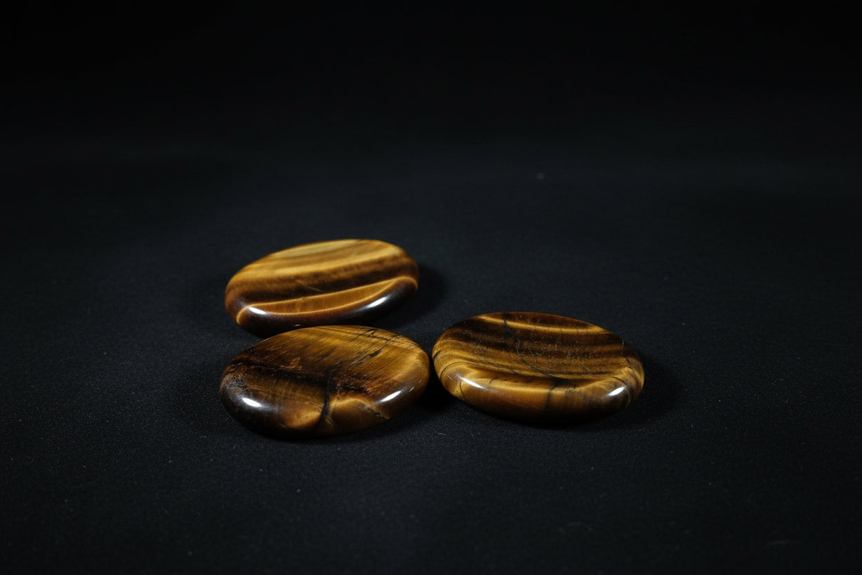 Assorted polished golden-brown tiger’s eye worry stones with varied chatoyant bands held in a hand