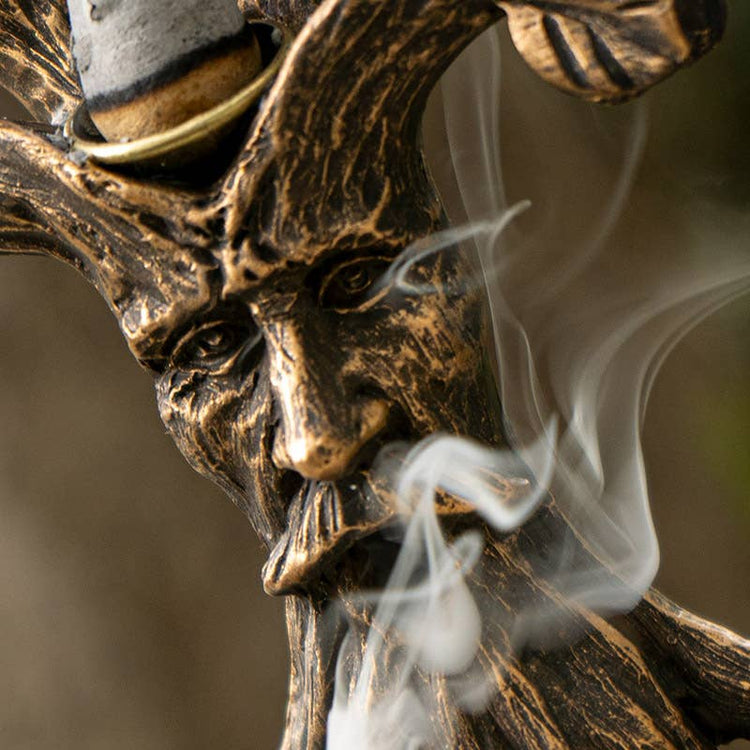Bronze tree of life statue of a face with smoke emerging from its mouth against a blurred background