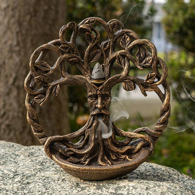Bronze tree-like sculpture with face on a rock outdoors