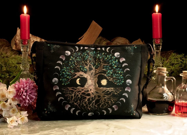 A black shoulder bag featuring the Tree of Life design with moon phases, displayed in a dimly lit environment with candles and floral decorations.