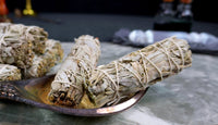 Bundles of white sage smudge sticks tied with string, displayed on a metal dish.