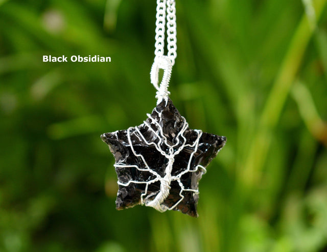 Black obsidian star-shaped pendant on a chain against a green blurred background