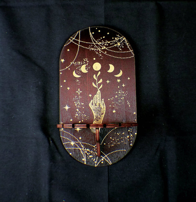 A wooden shelf with a pendulum holder featuring gold and white decorative patterns, mounted on a dark background.