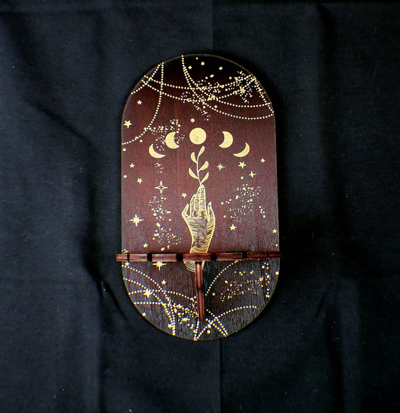 A wooden shelf with a pendulum holder featuring gold and white decorative patterns, mounted on a dark background.
