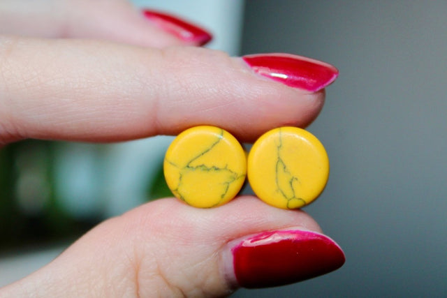 Yellow earrings held between fingers with red nail polish against a blurred background