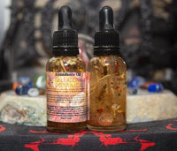 Two bottles of Abundance Oil with botanicals on a table with a blurred background